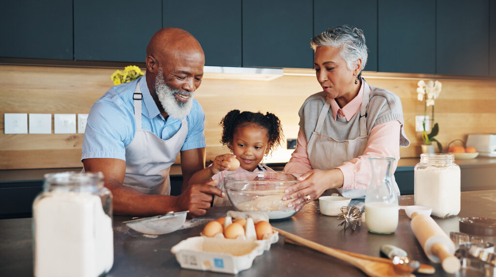 A man and woman with a mixing bowl between them with a child breaking an egg into the bowl